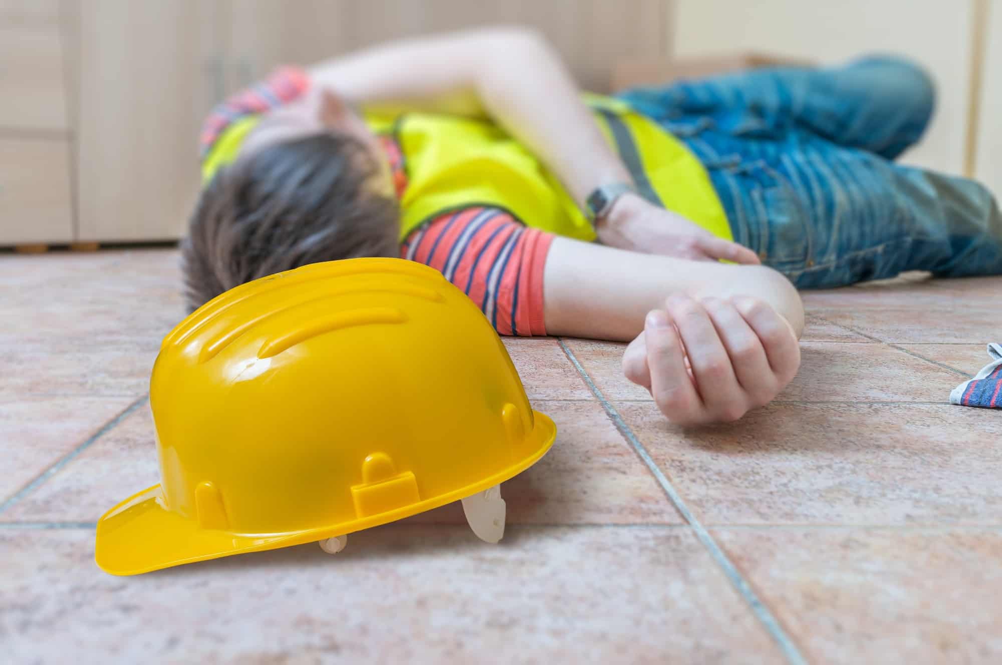 Injured worker had accident. Man is lying on the floor. Yellow helmet in front.