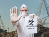 Technician In Coverall Warns In Landfill About Hazardous Waste.