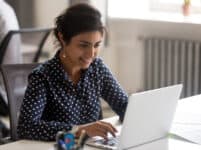 Smiling indian female employee using laptop at workplace